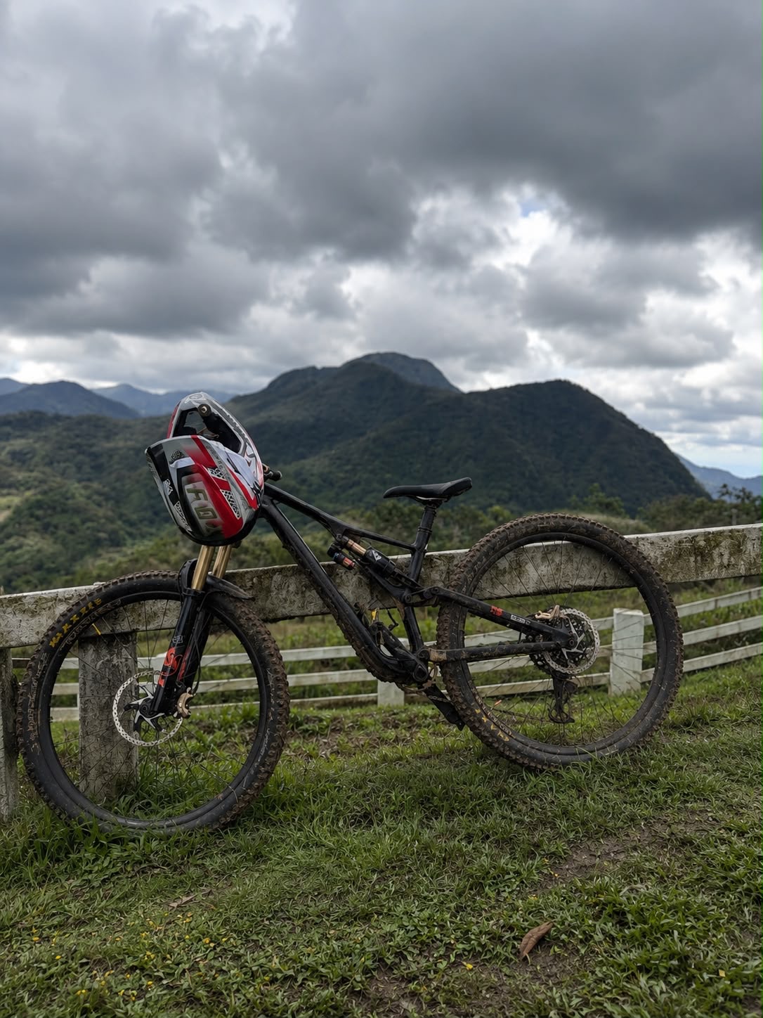Bicicleta embarrada apoyada en una cerca con montañas de fondo